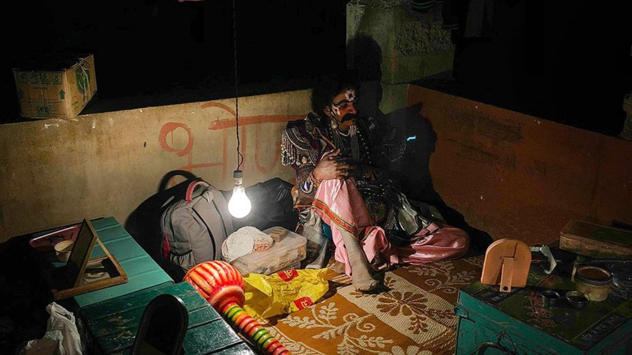 a man (Dashavtar Artist) sitting on the floor with a light bulb and think about his poor conditions